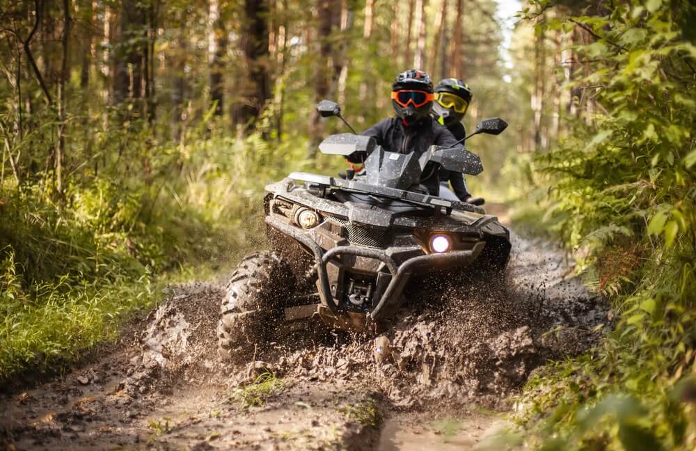Two people riding an ATV through mud on one of Broken Bow's trail